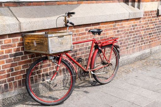 A red metal bicycle with an old wooden basket on a street leaning on a brick wall