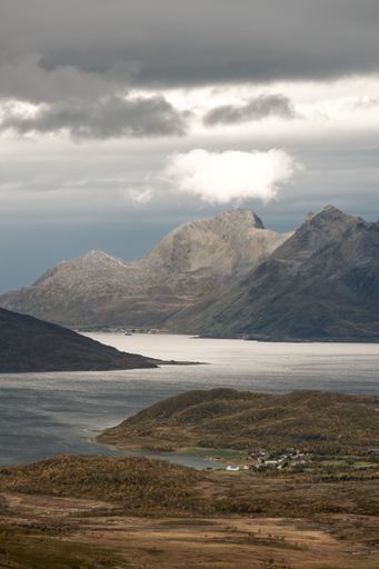 A vertical shot of a small town on the coast of a river with beautiful mountains in the background