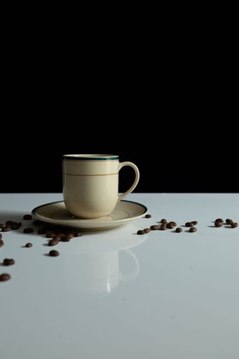 A vertical shot of a coffee cup and a plate on a reflecting table with scattered coffee beans
