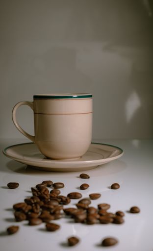 A vertical shot of a coffee cup and a plate on a reflecting table with scattered coffee beans