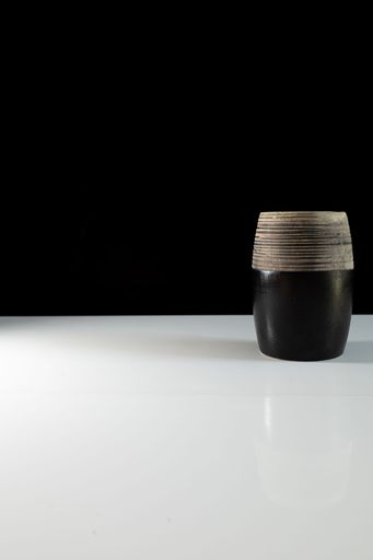 A vertical shot of a ceramic mug on a reflecting white surface on a black background