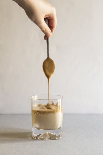 A vertical shot of a person stirring coffee with a spoon in a transparent cup on a white surface