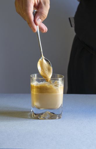 A vertical shot of a person stirring coffee with a spoon in a transparent cup on a white surface