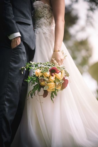 A newly married couple in embrace with the bridge holding a pretty bouquet in a vertical shot