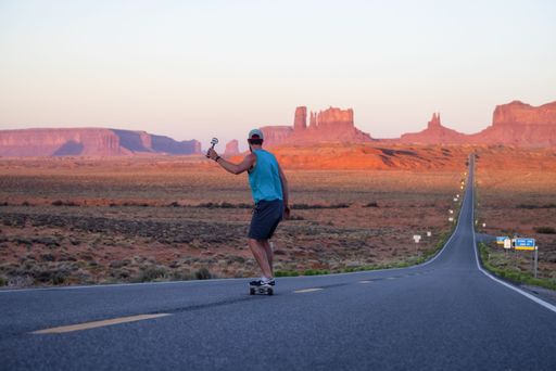 A man riding a skateboard down a road in the dry desert in Oljato-Monument Valley, Arizona, USA