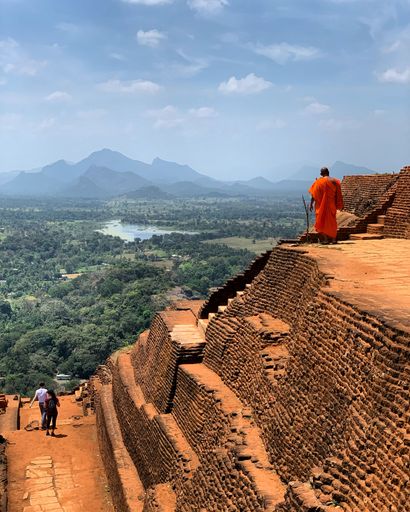 A vertical shot of a religious person standing on a rocky hill in cloudy sky background
