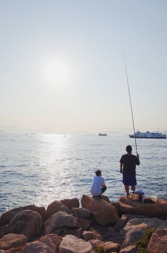 A vertical shot of two men trying to catch fish with a fishing nod in Hong Kong
