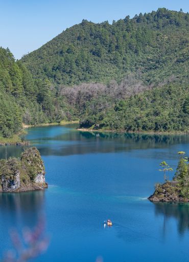 A vertical shot of a boat in Lake Tziscao with mountains covered in pine forests in the background, Mexica