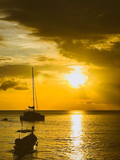 A vertical silhouette of a small Yacht anchored on the water with a beautiful red sky after the sunset