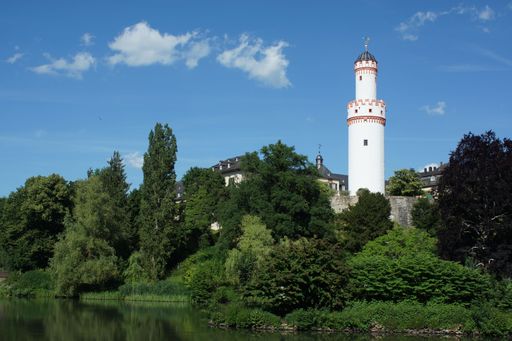 Keep of Bad Homburg Castle, Germany. The white tower framed by green trees against blue summer sky above the park lake. A tourist attraction.