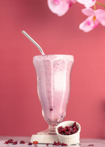 A vertical shot of glass of cranberry milkshake with small bowl of dried cranberries