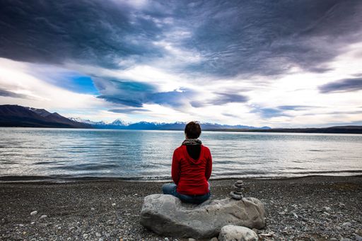 A rear view of a person sitting on a rock looking at the Lake Pukaki in New Zealand