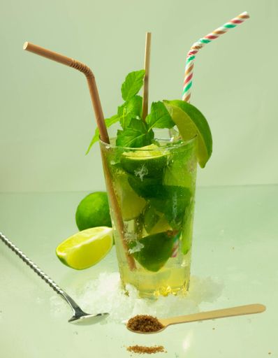 A vertical shot of a mojito cocktail with rum, lime and mint leaves on a light green surface