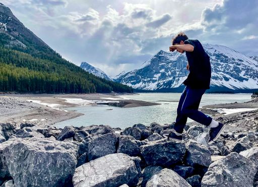 A boy jumping on the rocks near a calm lake in Kananaskis, Alberta, Canada