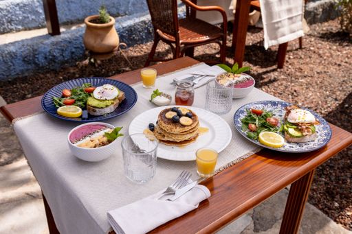 A high angle of a delicious brunch with pancakes and avocado toast on a wooden table with chairs in the background.
