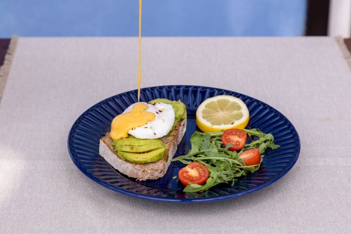 An avocado toast and salad served on a blue plate with a yellow sauce falling on it.