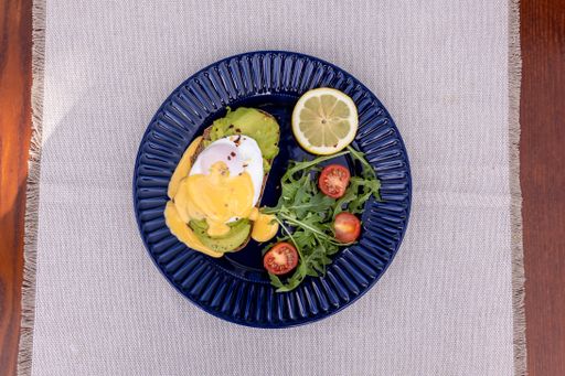 A top view of an avocado toast with salad served on a blue plate.