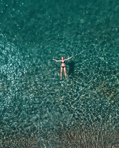 A woman swimming in clear blue water at a beach in Greece during summer.