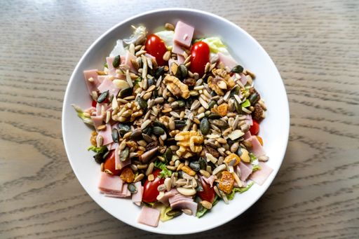 A high angle shot of a salad with vegetables and ham on the white plate