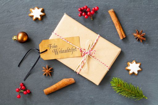 A top view of a gift box with a "Frohe Weihnachtsfest - Merry Christmas" tag on it on the table with decorations
