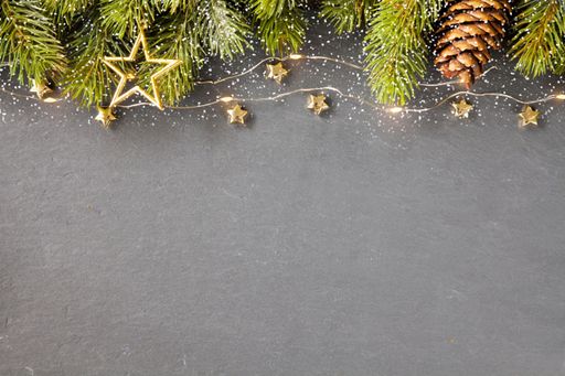 A top view shot of Christmas tree branches with gold ornaments and a pine cone on a gray background