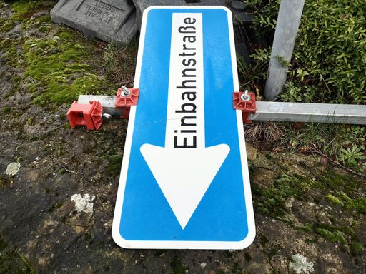 A fallen blue traffic sign with 'One way street' in German written on it