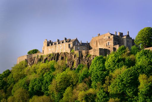 The low-angle view of Stirling Castle on top of the green cliff under the blue sky