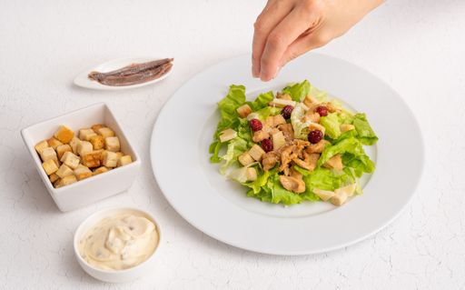 Salad with toasts, anchovies and sauce on white plate and white background with cracks