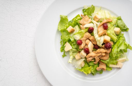 Salad with toasts, anchovies and sauce on white plate and white background with cracks