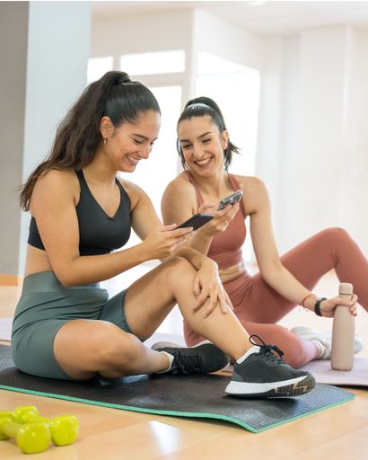 TWO GIRLS DOING PILATES AND YOGA, WHILE ONE IS ON THE PHONE AND ANOTHER DRINKS WATER rey happy