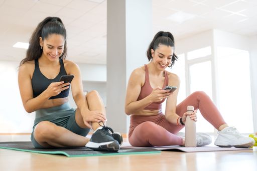 TWO GIRLS DOING PILATES AND YOGA, WHILE ONE IS ON THE PHONE AND ANOTHER DRINKS WATER rey happy