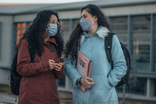 A pair of female student friends with COVID masks and jackets walking around on college campus