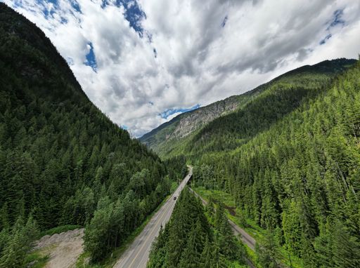 An aerial of a road through the green mountains under a cloudy sky.