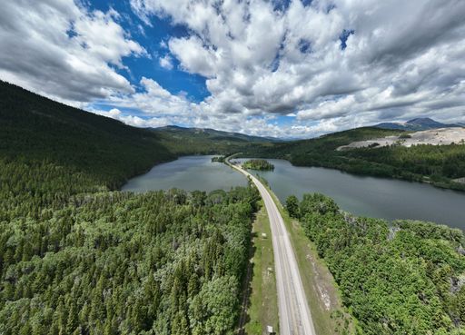 An aerial of a road and a river surrounded by green mountains under a cloudy sky.