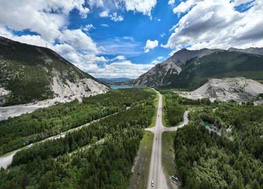 An aerial of a road and a river surrounded by green mountains under a cloudy sky.