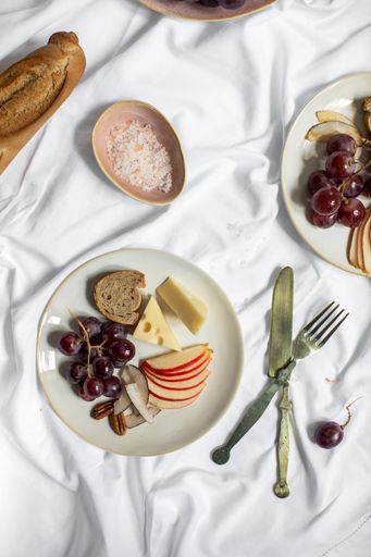 A vertical shot of breakfast table with snacks, bread, cheese and fruits on a white surface