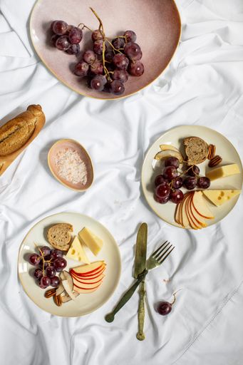A vertical shot of breakfast table with snacks, bread, cheese and fruits on a white surface
