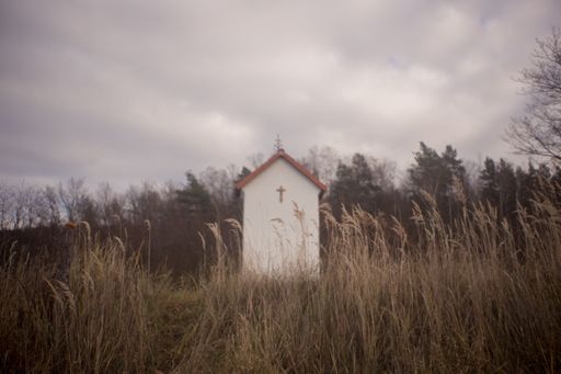 A white chapel in a grassy field surrounded by green trees under the breathtaking cloudy sky
