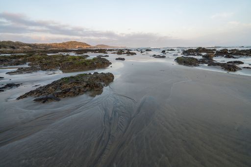 A beautiful view of a sea shore with big rocks under cloudy blue sky