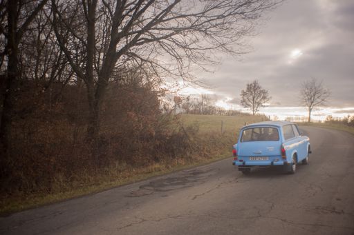 A blue trebant driving through the czech country side after a rainy day.