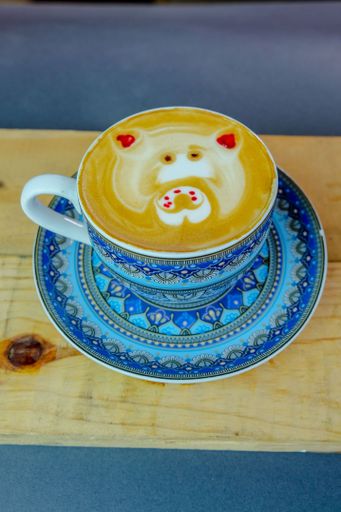 A vertical shot of a Cappuccino with a pig art on a wooden tray on the table