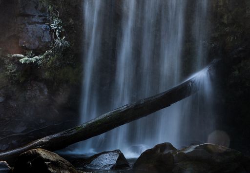 A dark shot of a strongly falling waterfall flowing on rocks and splashing on a wooden stick