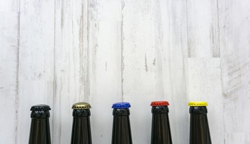 A closeup of dark beer bottles with colorful caps on a wooden surface