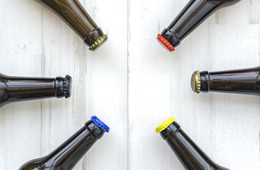 A top view of glass beer bottles with colorful caps on a wooden surface
