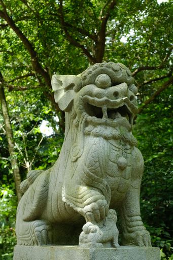 A vertical shot of Japanese stone lion statue in the park with green trees in the background