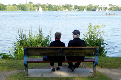 A back view of senior couple sitting on wooden bench on the shore of Outer Alster lake in Germany