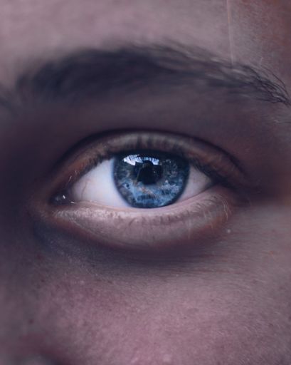 A closeup shot of a beautiful blue eye with the reflection of the photographer in the pupil