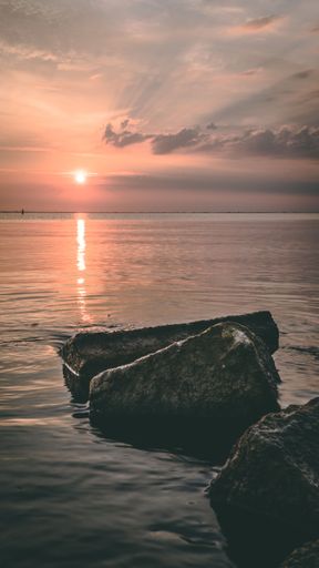 The bright sunset sun in pink sky shining over the large stones near the shore in Almere
