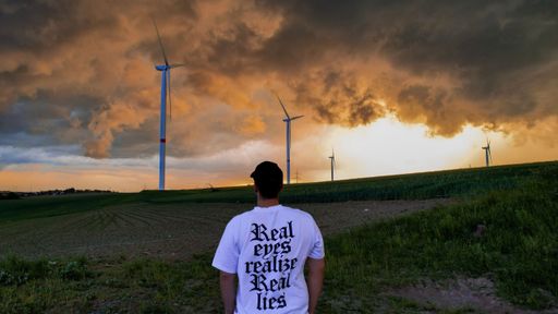 A back shot of a male standing on a green field looking at a dramatic sunset sky
