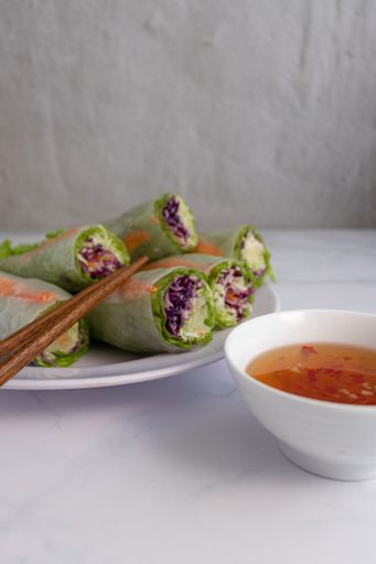 A vertical shot of Vietnamese spring rolls with fish sauce dip on a white table